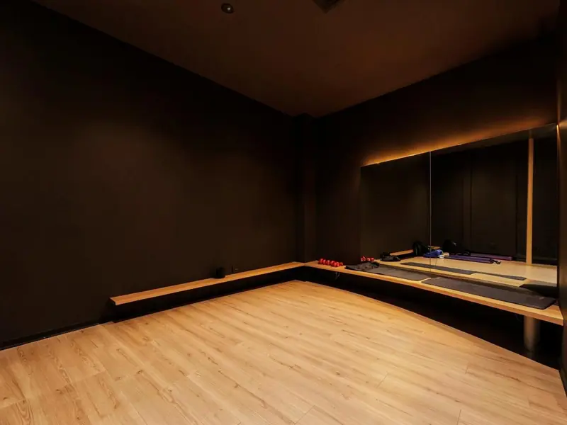 Empty movement studio with a pale wood floor, mirrored wall and warm light along the ceiling
